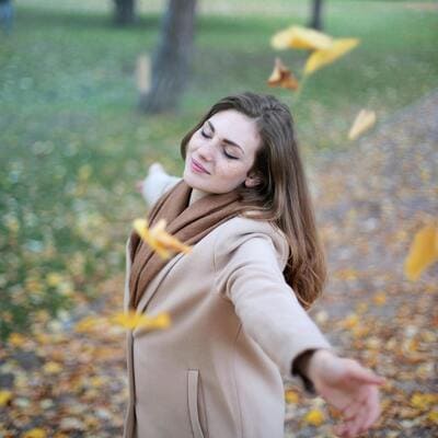 Mulher feliz com os braços estendidos entre folhas caindo, simbolizando a alegria proporcionada pela inteligência emocional.