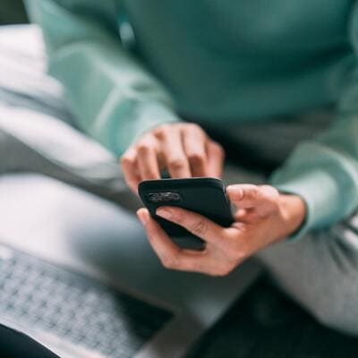 Pessoa segurando um smartphone com um laptop ao fundo, simbolizando as adições modernas e seus impactos na saúde mental.