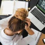 : Mulher em um escritório, segurando a cabeça com uma das mãos, simbolizando estresse ou concentração em um ambiente de trabalho.