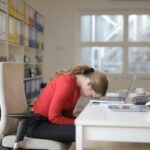 Pessoa exausta em uma mesa de trabalho com laptop e itens de escritório, simbolizando burnout e sobrecarga emocional.
