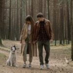 Casal caminhando juntos com seu cachorro em uma floresta, simbolizando o compartilhamento de responsabilidades no relacionamento.