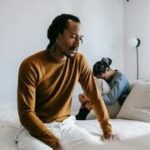 Casal sentado na cama, expressando dificuldades emocionais em lidar com o perdão no relacionamento.