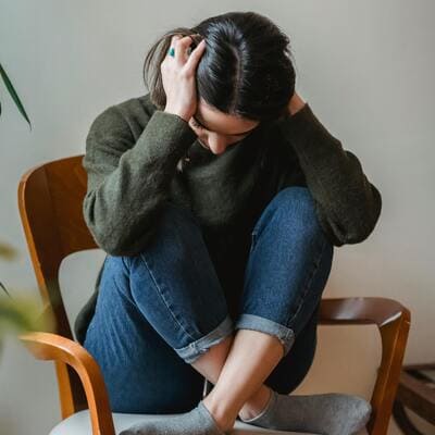 Mulher sentada em uma cadeira com as mãos na cabeça, simbolizando os desafios emocionais do transtorno de estresse pós-traumático (TEPT).