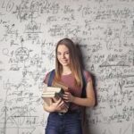 Mulher estudiosa segurando livros em frente a um quadro com equações, simbolizando inteligência emocional e busca por conhecimento.