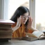 Mulher estudiosa lendo livros em uma mesa iluminada, simbolizando inteligência emocional e busca por conhecimento.