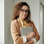 Mulher inteligente segurando um laptop em um ambiente interno, simbolizando inteligência emocional e profissionalismo.