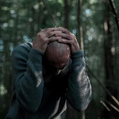 Homem em pânico na selva, cercado por árvores, simbolizando medo e desafios emocionais.