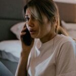 Mulher em pânico segurando um telefone, sentada em uma cama, simbolizando medo e desafios emocionais.