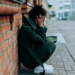 Pessoa em pânico, agachada em um canto com um telefone na mão, simbolizando medo e isolamento emocional.
