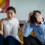 Casal sentado no sofá discutindo, simbolizando problemas de comunicação em um relacionamento.