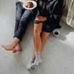 Casal sentado no chão de madeira, aproveitando um momento casual que simboliza rotina e desgaste no relacionamento.