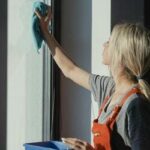Mulher limpando obsessivamente uma janela com um pano, simbolizando comportamentos compulsivos relacionados à limpeza.