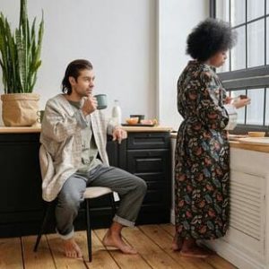 Mulher cozinhando sozinha enquanto o homem mexe no celular, simbolizando o desequilíbrio de responsabilidades no relacionamento.