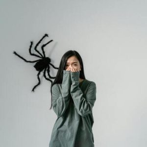 Mulher em frente a uma grande aranha decorativa na parede, simbolizando fobias e enfrentamento terapêutico.