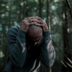 Homem em pânico na selva, cercado por árvores, simbolizando medo e desafios emocionais.